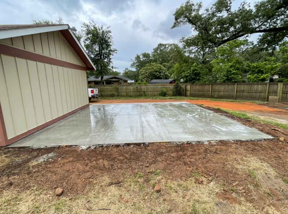 A covered concrete deck in the backyard emerges as a versatile oasis, offering both shelter and open-air freedom, where relaxation meets the embrace of nature